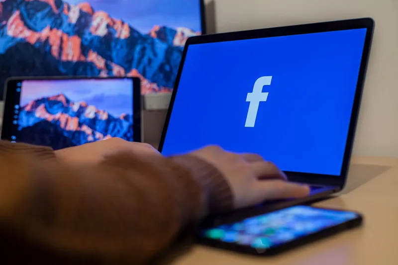 Laptop and devices at a workspace showing multiple social media platforms open side by side