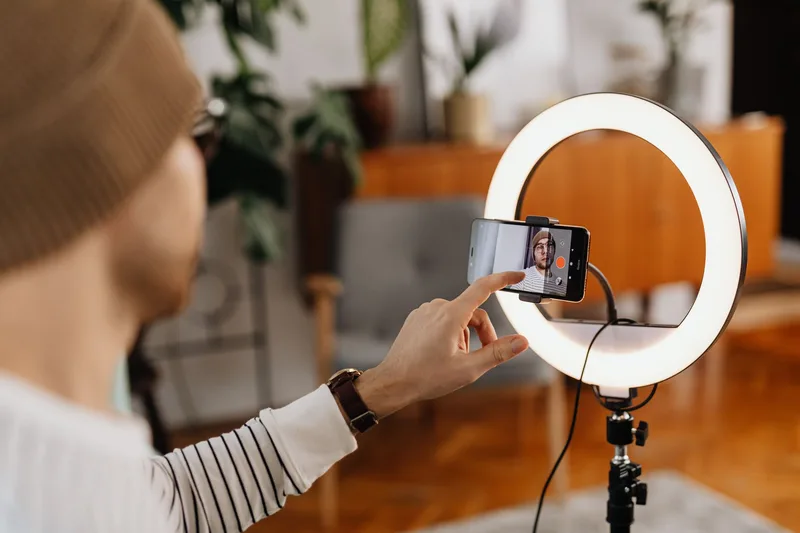 Adult creating video content with smartphone and ring light in a cozy indoor setting