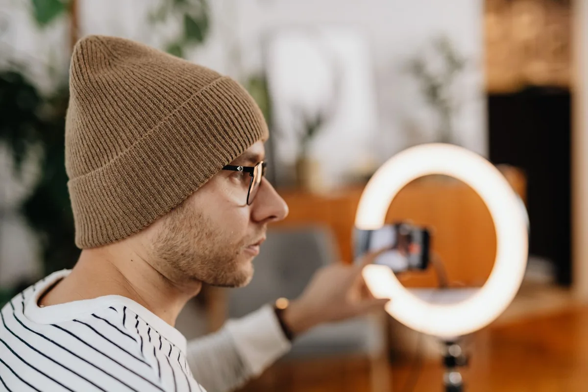 Creator wearing headphones and recording TikTok video content indoors using a smartphone and ring light
