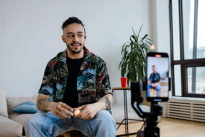 Young man recording social media video content indoors with a smartphone and tripod in a home setup