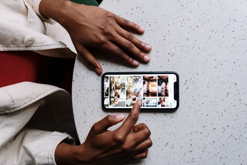 Close-up of hands scrolling through a grid of photos on a smartphone