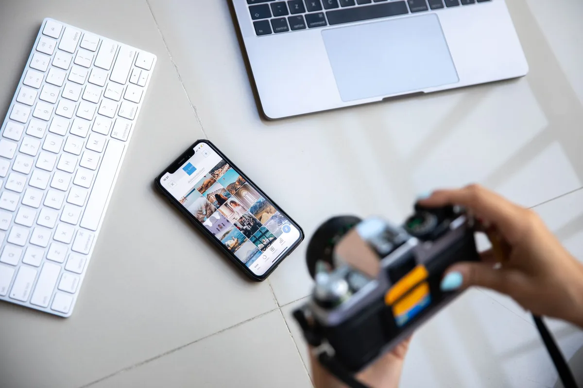 Creator reviewing a grid of photos on a smartphone next to a camera and laptop