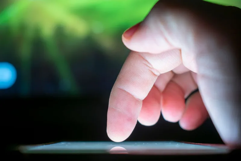 Close-up of a finger tapping a glowing smartphone touchscreen