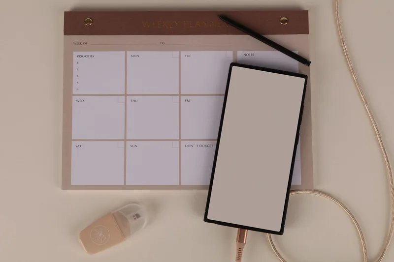 Flat lay of a minimalist desk setup with a weekly planner and smartphone for scheduling posts