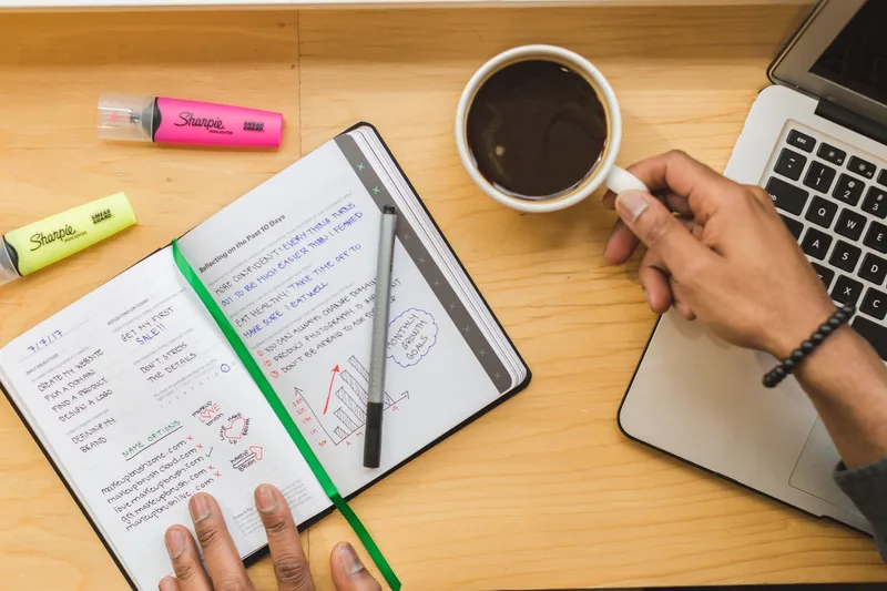 Overhead view of a notebook, coffee, and laptop on a desk, representing scheduling and batching YouTube Shorts uploads