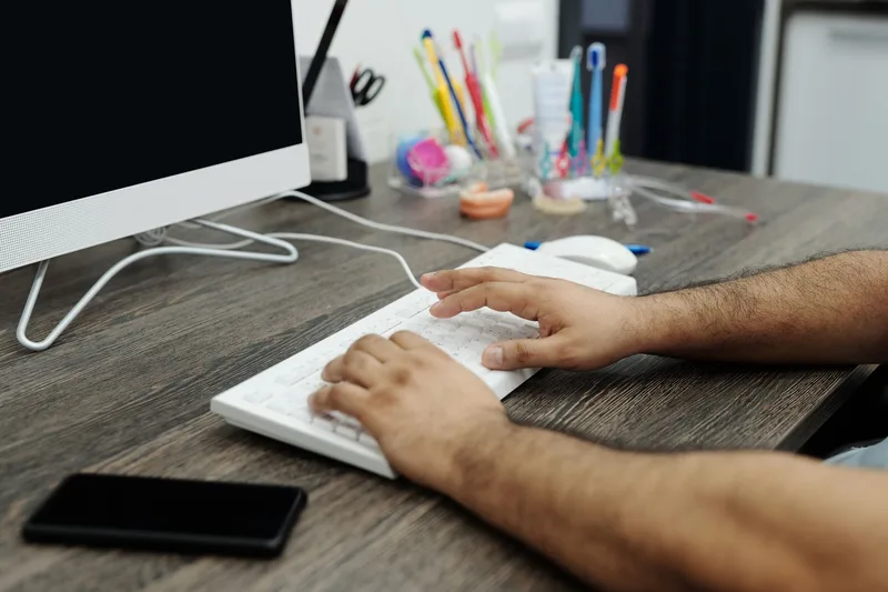 Close-up of hands typing on a white keyboard at a desk, representing a creator building and managing their Instagram content scheduling workflow
