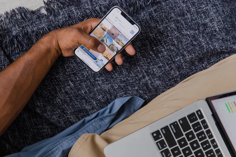 Hand holding a smartphone next to an open laptop, representing a multi-device social media scheduling workflow