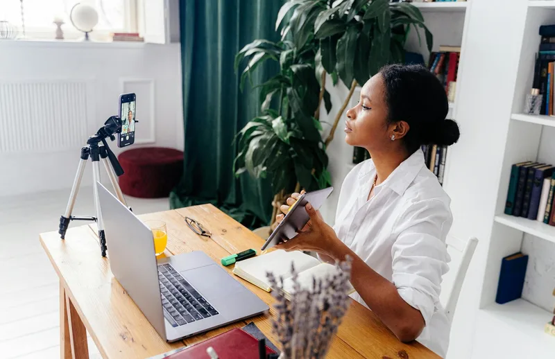Content creator using laptop and devices at home desk workspace for creating and sharing content